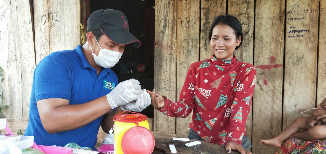 Mobile malaria worker wearing PPE holds woman's finger