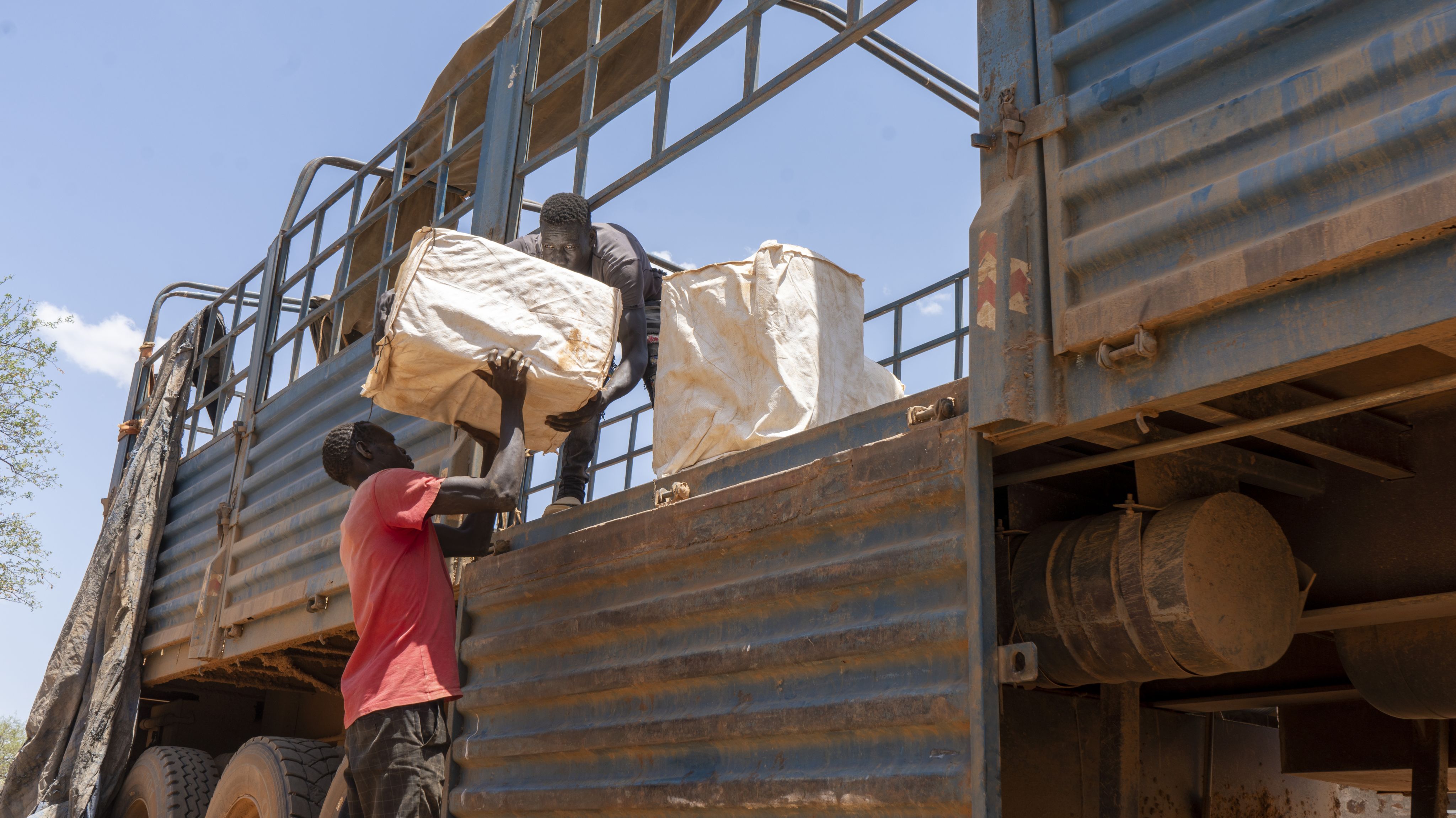 Two men unload large white sack off lorry