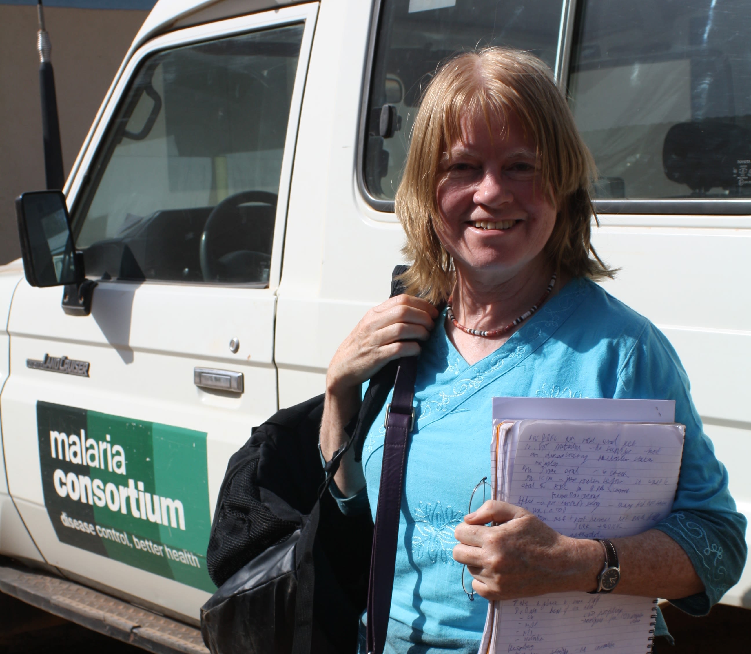 Woman holding papers stands smiling beside white truck