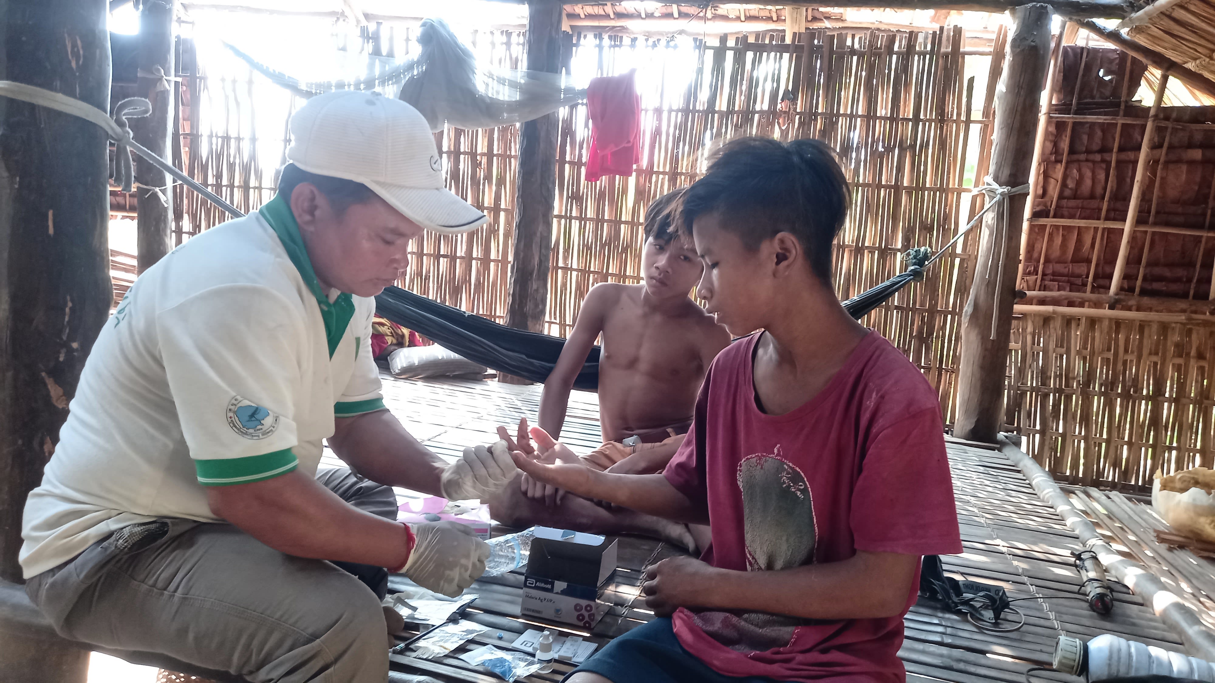 Healthcare worker holds boy's finger as tests for malaria with young boy watching