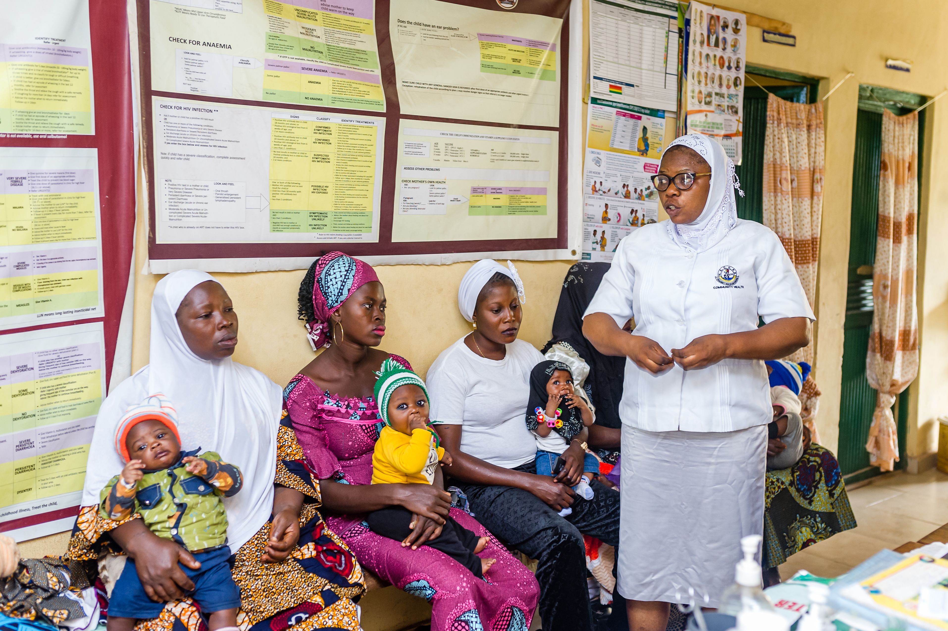 Healthcare worker speaks to group of seated women holding young children