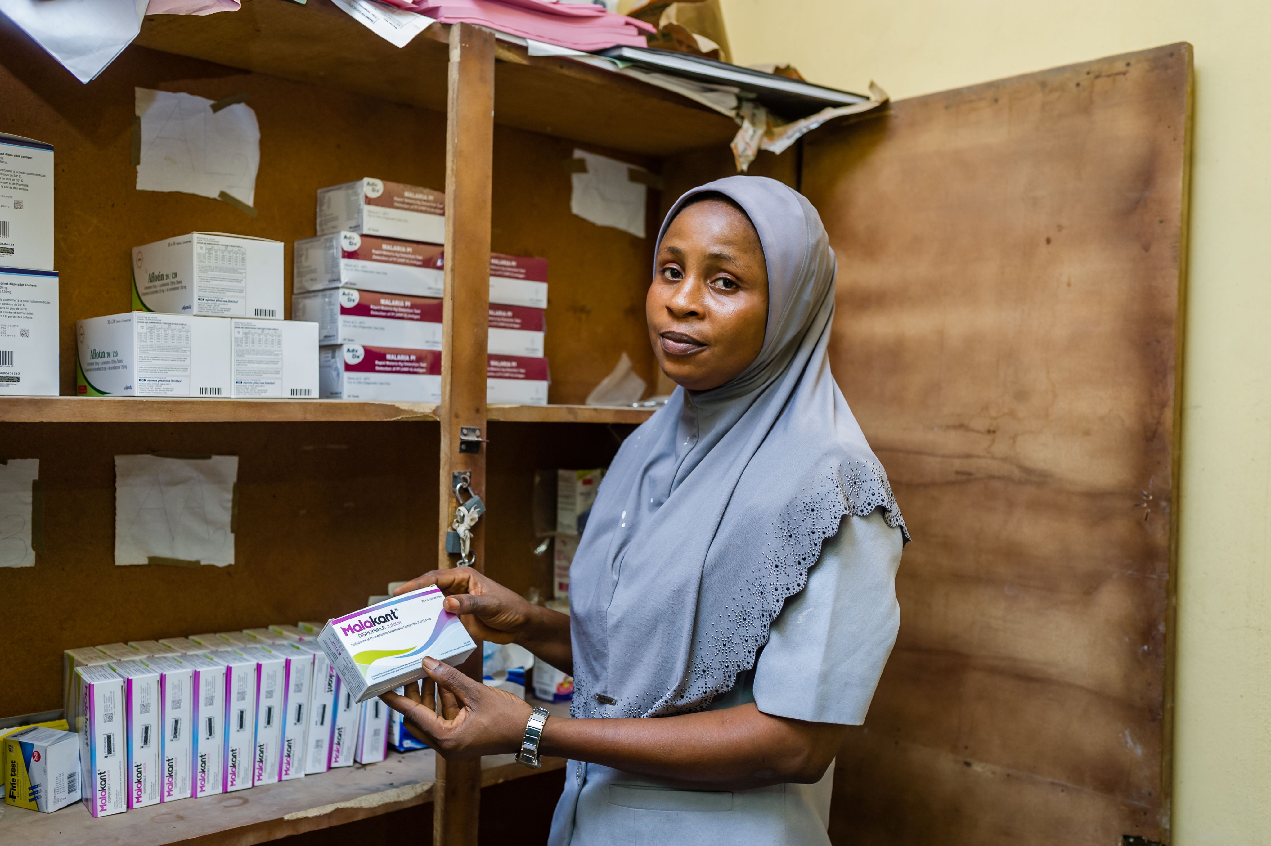 Woman stands beside shelves of medicines holding a box of tablets