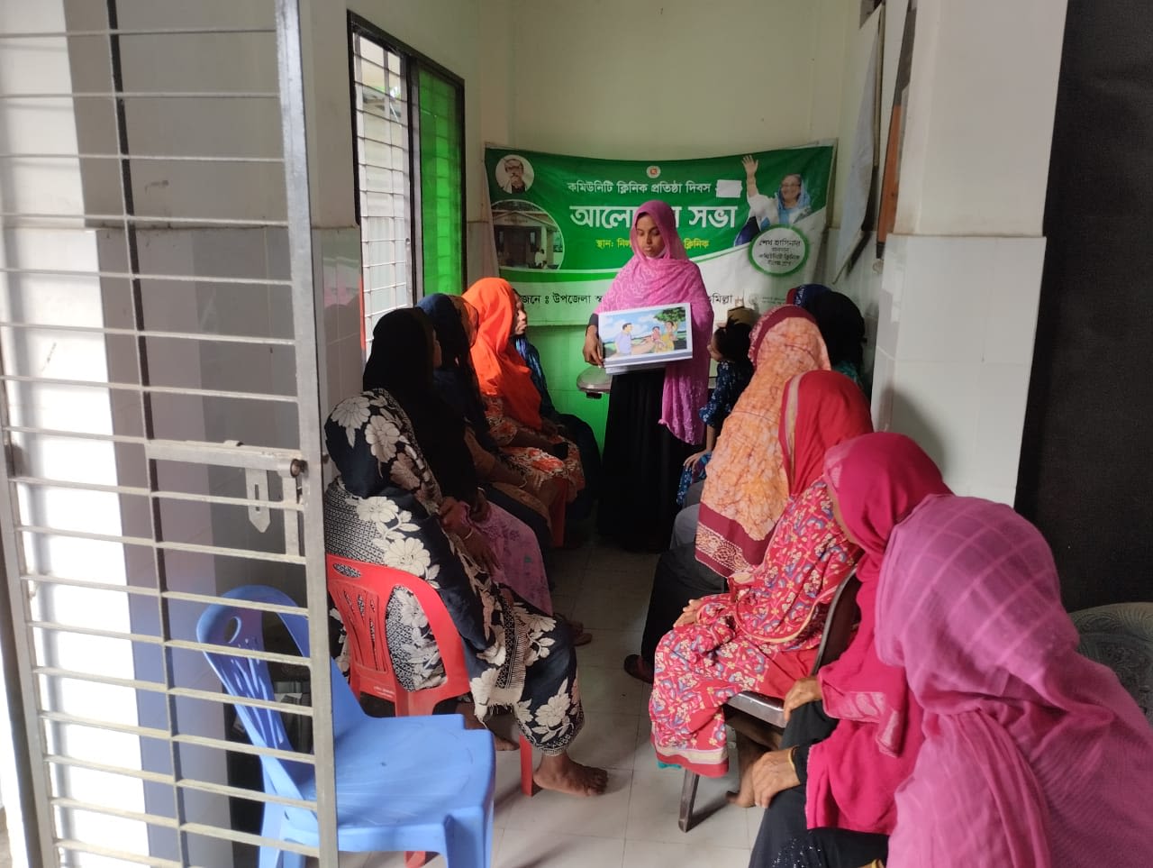 Woman stands holding visual aid and talks to group of seated women
