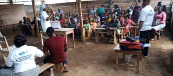 Community health worker talks to group of people sat at desks