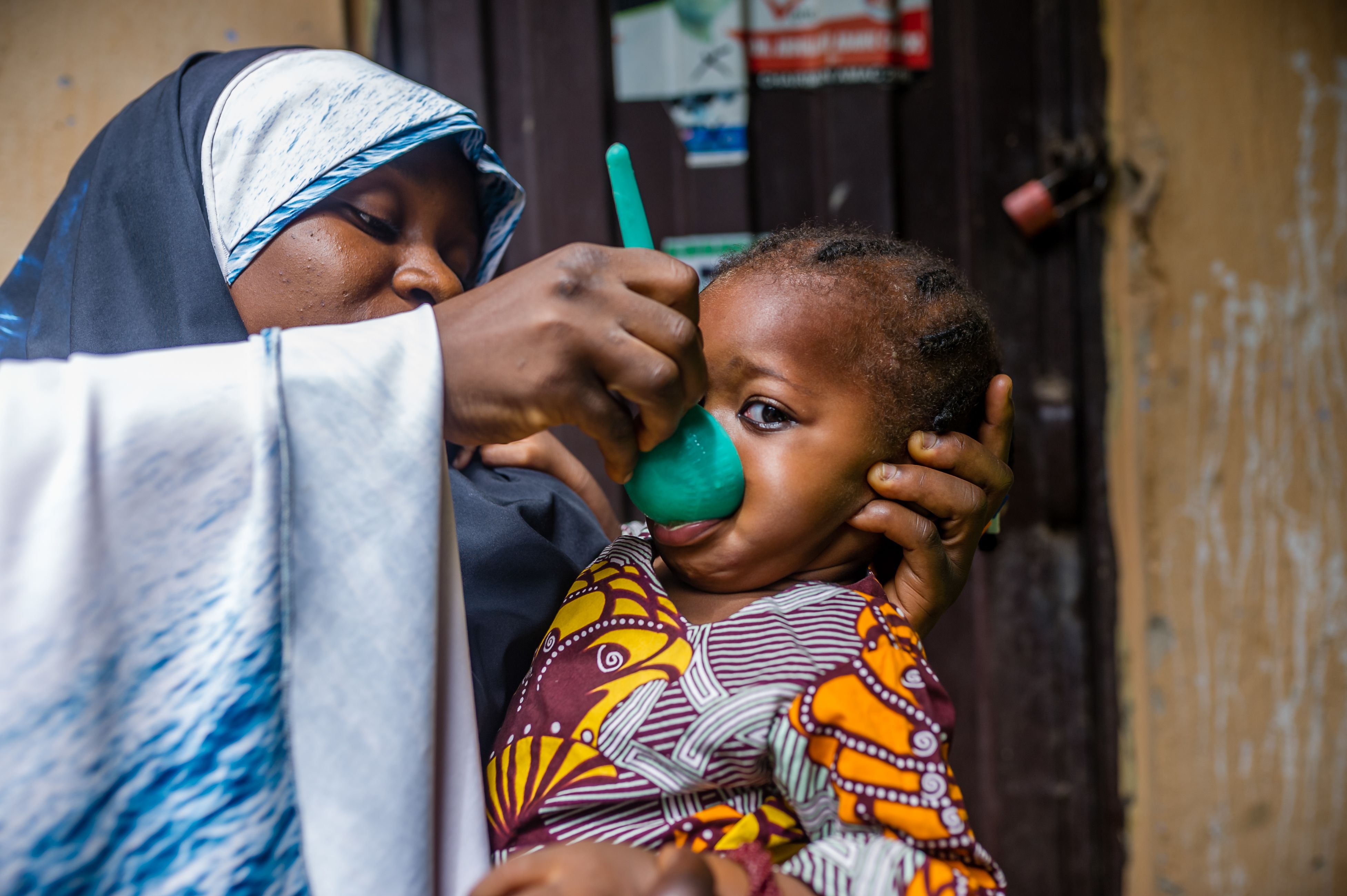 woman pours medication into small child's mouth from plastic scoop