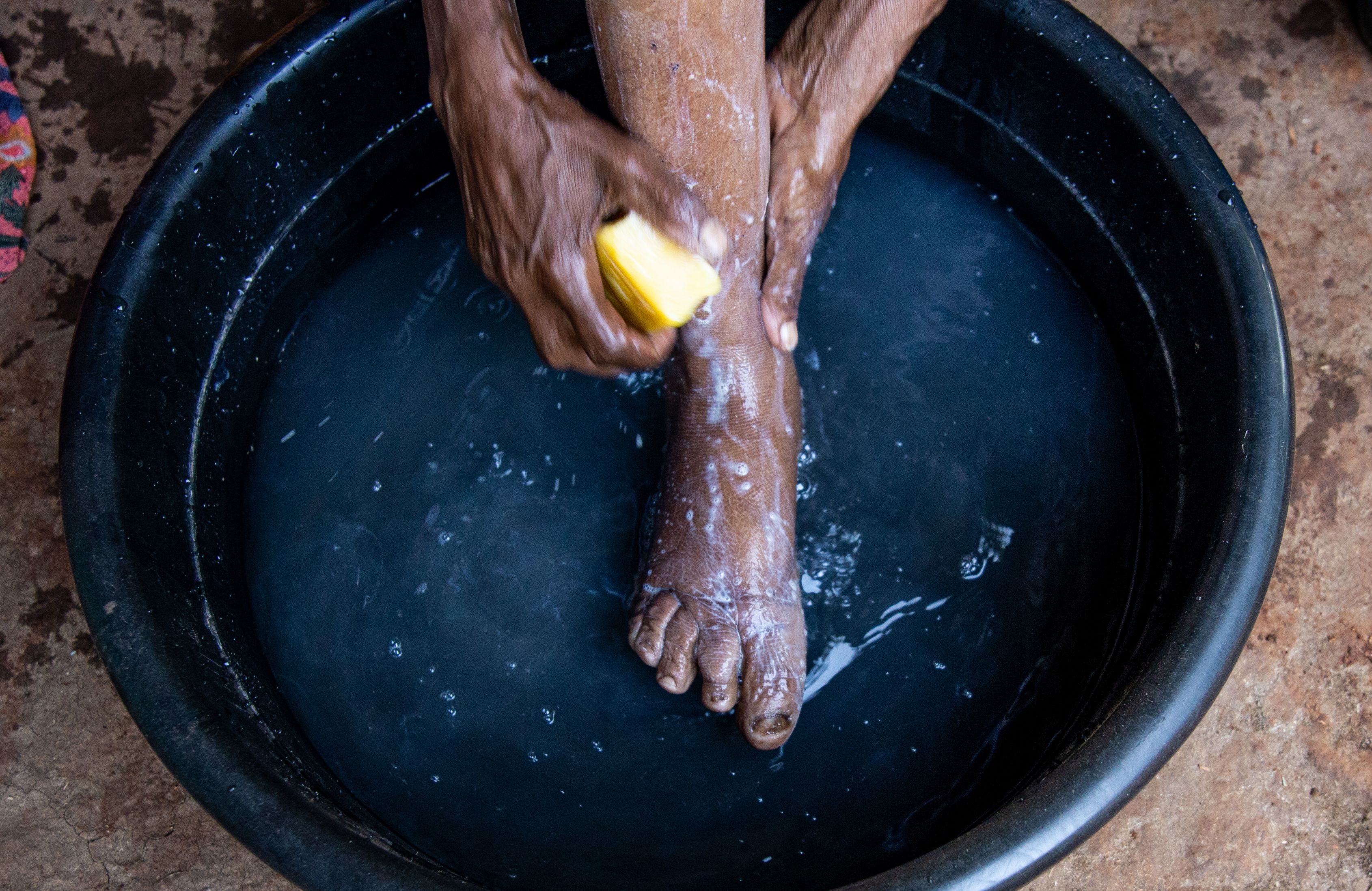 Feet in a bowl of water being washed with soap