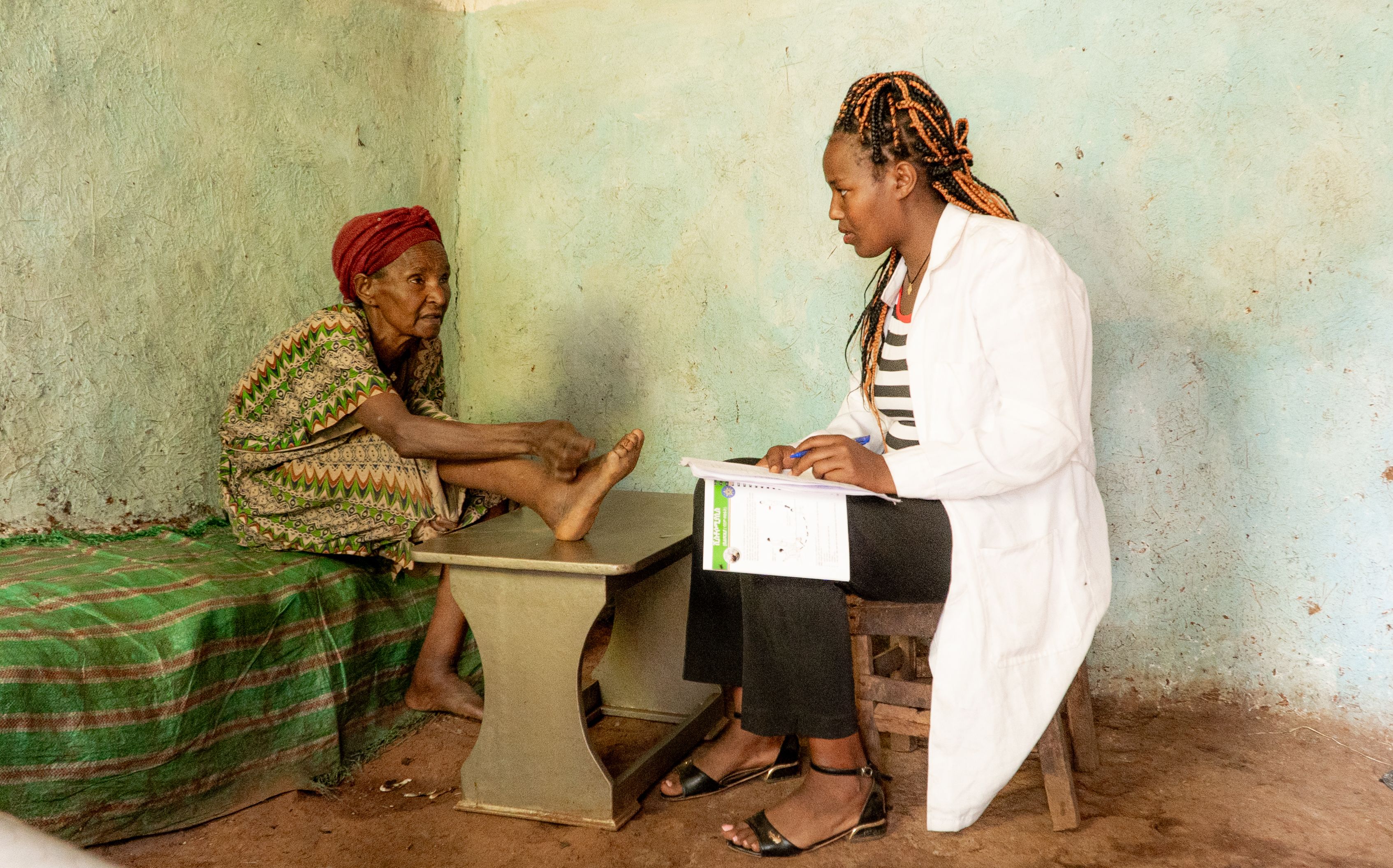 Woman with podoconiosis sits with her foot on a table as healthcare worker talks to her