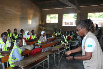 Woman speaks to group of community distributors sitting at desks