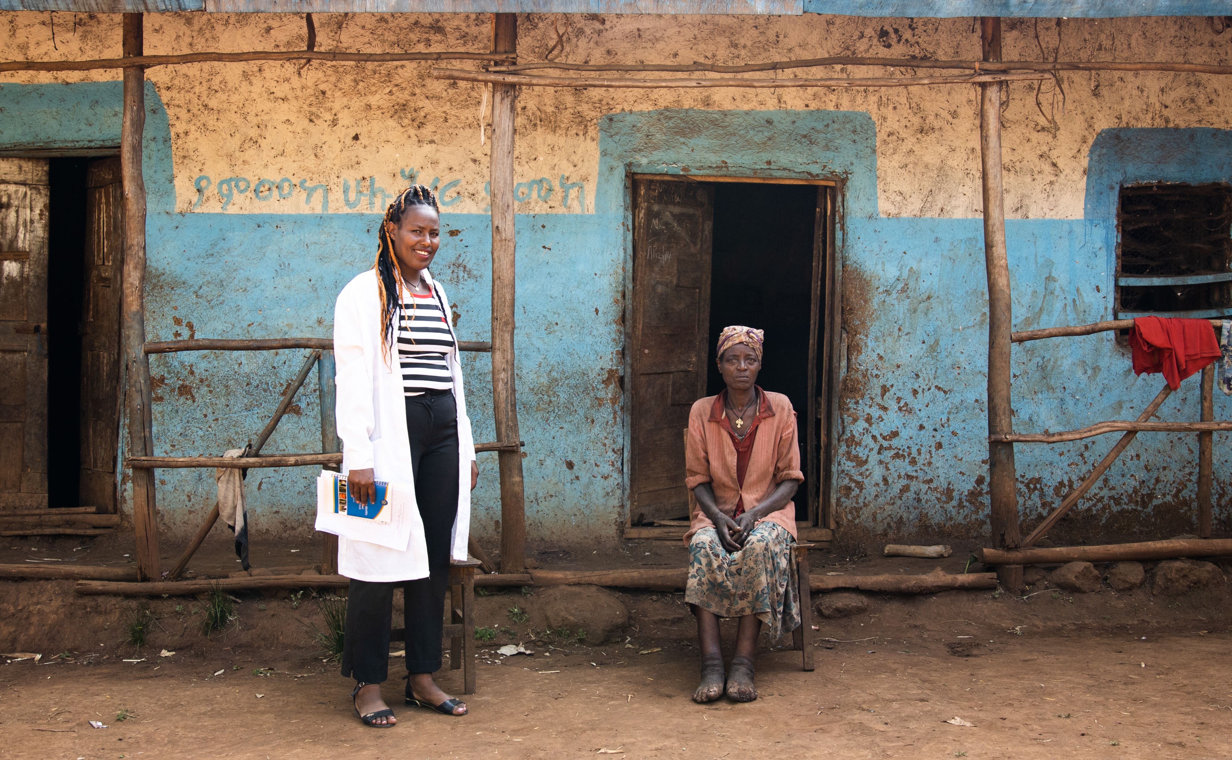 Heathcare worker stands beside seated woman who is barefoot and has podoconiosis