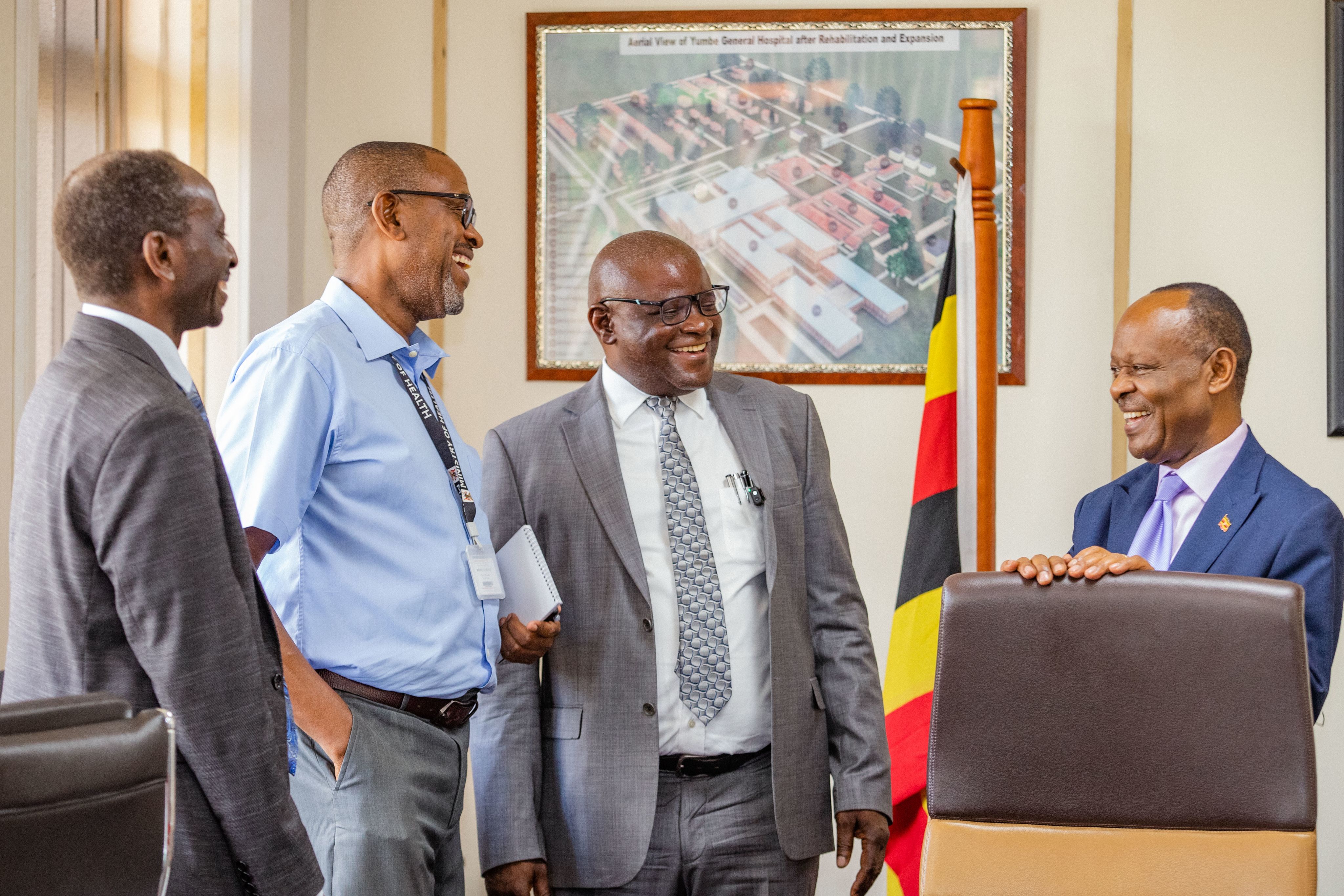 Four men stand smiling and talking in a government office