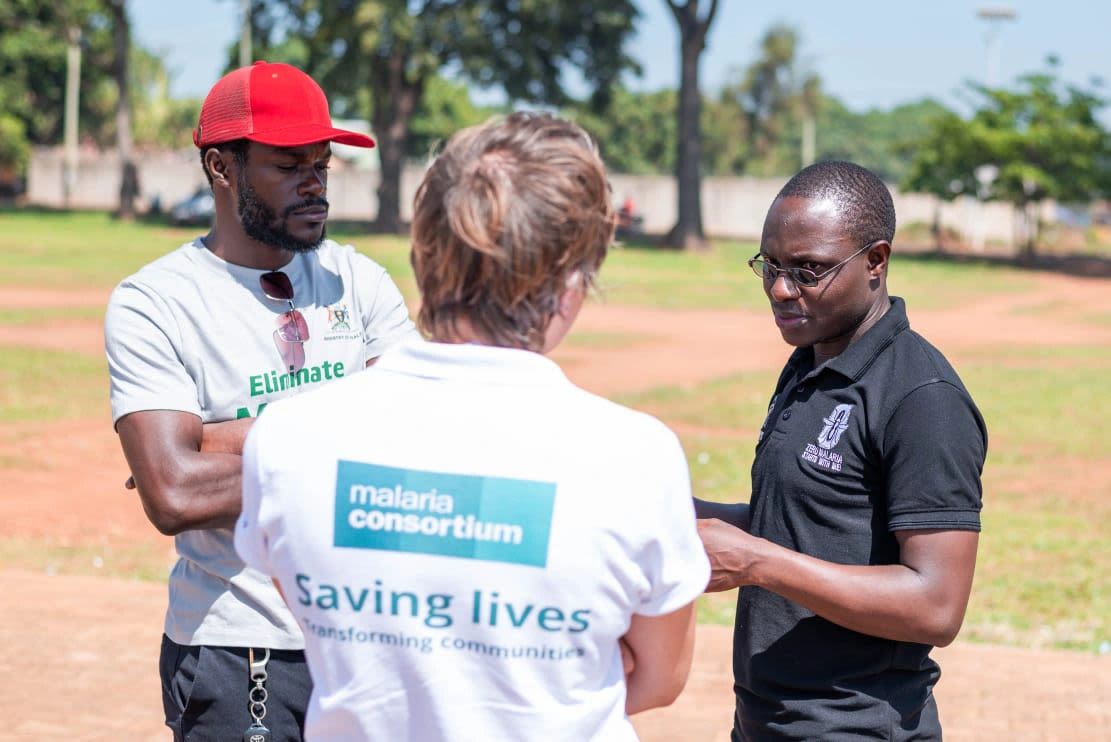 Woman with her back to the camera stands talking to two men