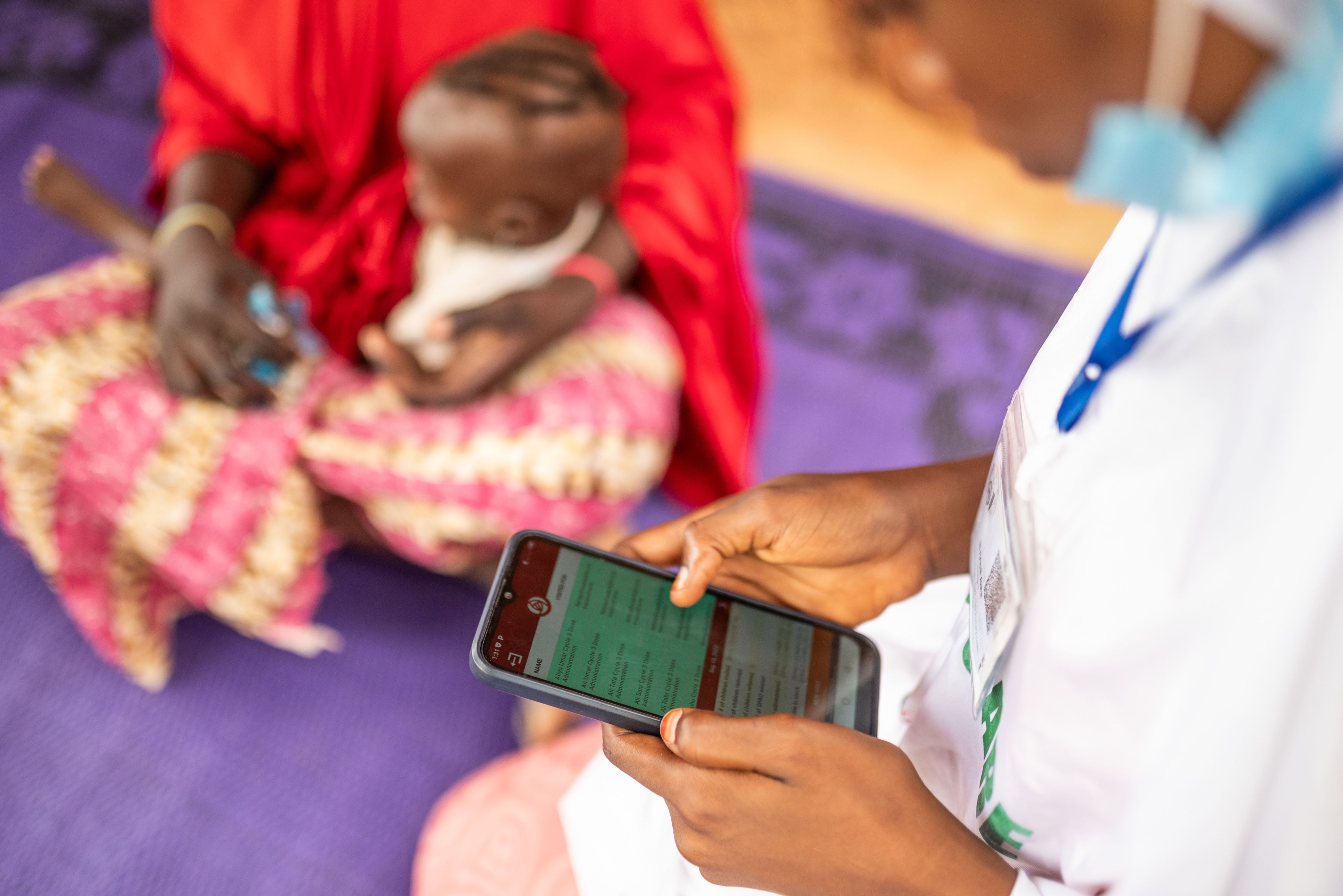 Person uses smartphone while person sitting with small child sits in the background